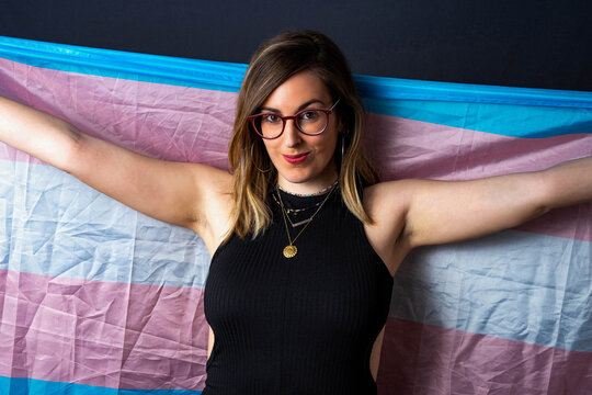 Brunette Haired Transsexual Woman with Glasses and Necklaces Holding a Transgender LGBT Flag with Op