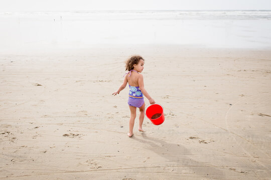 Girl in swimsuit carries bucket to ocean
