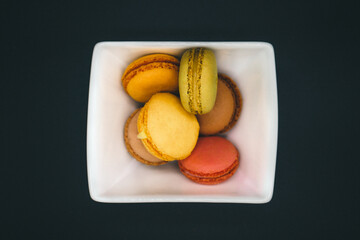Macarons de colores de postre en un plato blanco con fondo negro
