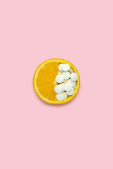 Creative food health diet concept photo of orange slice with medical pills vitaamins on pink...