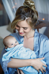 Young beautiful mother with her cute little baby wrapped in the blue cloth