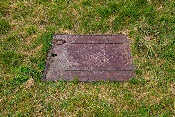 Close up of a old rusty metal square hatch in a grass field