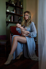Obraz premium Young beautiful mother wearing luxury grey dress holding her baby on hands