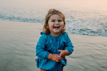 Adorable laughing girl in blue swimsuit wading in the ocean at sunset
