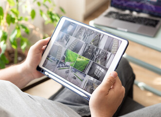 man hands holding digital tablet with multiple camera views of office locations. Surveillance...