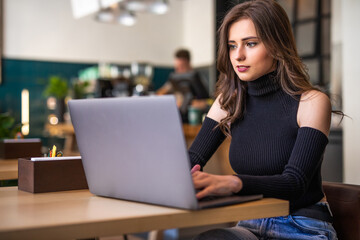 Beautiful young woman working on laptop and smiling while sitting in cafe