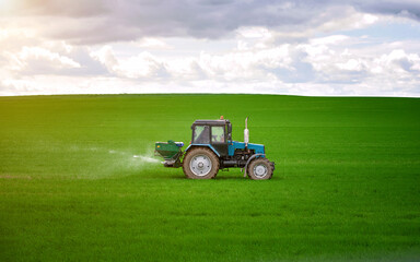 Tractor spreading potash fertilizer on green wheat field. Agriculture vehicle spraying field. Tractor spray fertilizers on green field, agriculture wallpaper. Farmer spreading potash fertilizers.