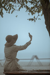 Fototapeta premium Rear view of young woman woman wearing hat a holding smart phone
