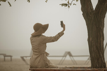 Foggy morning at sea. Woman in hat and coat walking near autumn foggy sea