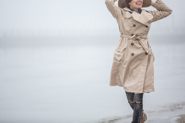 Foggy morning at sea. Woman in hat and coat walking near autumn foggy sea