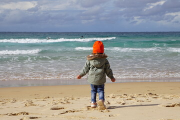 Child is looking on big ocean waves.