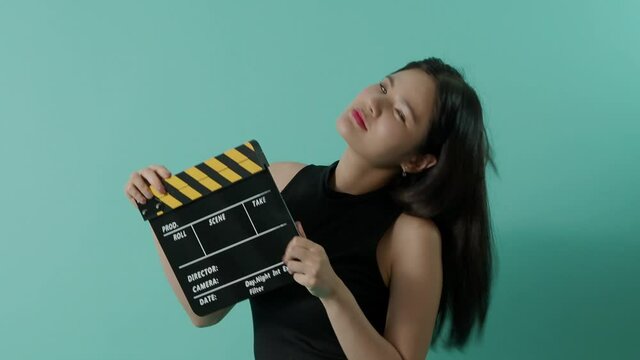 Movie slate and little sexy cute asian girl. Woman holding and clapping movie clapperboard or film slate with green screen background. Camera zooming in and out to show her smile. video production.