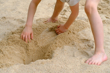 child plays in the summer with sand on the playground, in the sandbox, the concept of the development of fine motor skills, creativity, building sand castles, summer vacation, fun on the beach