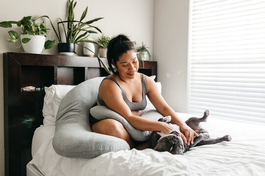 A portrait of a pregnant African American woman playing with her french bulldog on the bed. 