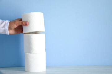 A woman holds a roll of toilet paper. A stack of rolls of white toilet paper on a blue background. Pattern.