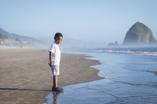 Happy boy stands at ocean's edge on beach