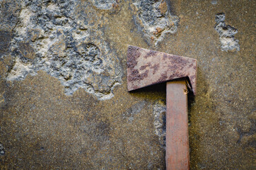 The picture of an old ax placed on a rough concrete surface, the ax is made of iron and has rust stains. The handle is made of wood materials.