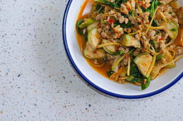 A picture of hot and spice red curry with minced pork and vegetables such as small eggplant, fingerroot, chili peppers, kaffir lime leaves, placed in a serving dish.
