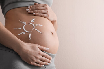 Pregnant woman with sun protection cream on her belly against beige background, closeup. Space for...