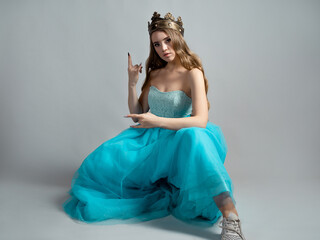 Fototapeta premium Cool princess in a lush blue dress and crown makes a rocker hand gesture,