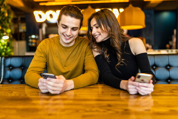 Happy couple using smartphone together and drinking coffee in cafe