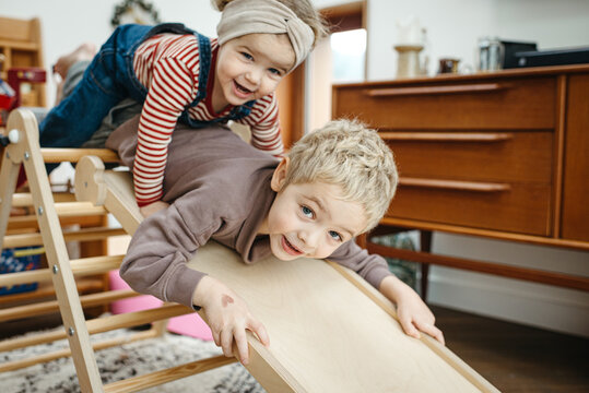 Toddler boy and sister enjoying climbing and sliding on a pikler triangle