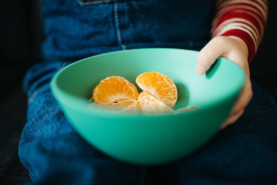 Close up of a green bowl with clementine pieces held by toddler