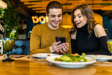 Couple in restaurant eating lunch and looking on smartphone