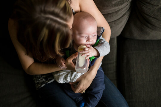 Young mom feeds baby bottle as he looks away