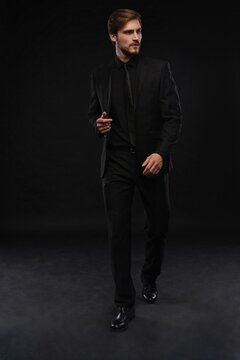 Young man in black suit full body portrait against black background.