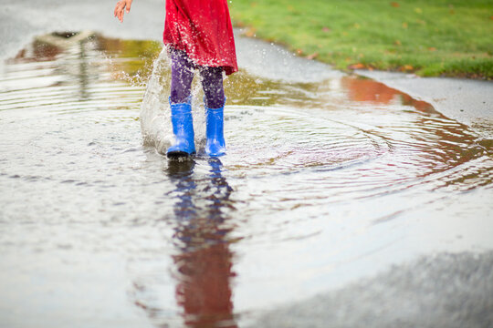 Child in dress and boots stomps through puddle