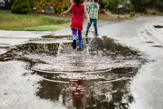 Girl chases brother through puddle 
