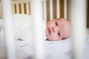 alert baby peeks through bars of crib