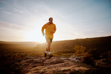 Fit young male athlete returning back after morning run on mountain trail