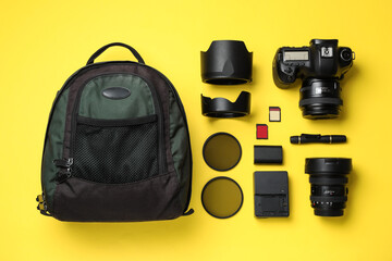 Backpack, camera and professional photographer's equipment on yellow background, flat lay