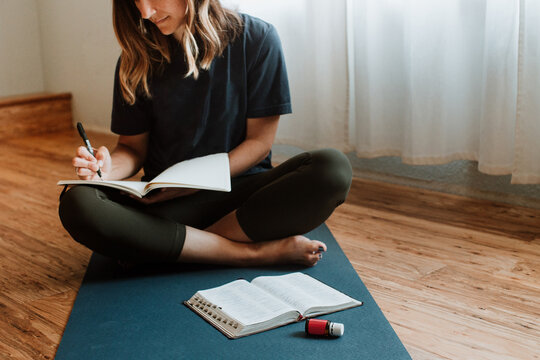 Woman In Background Journaling With Bible And Essential Oil In Foreground