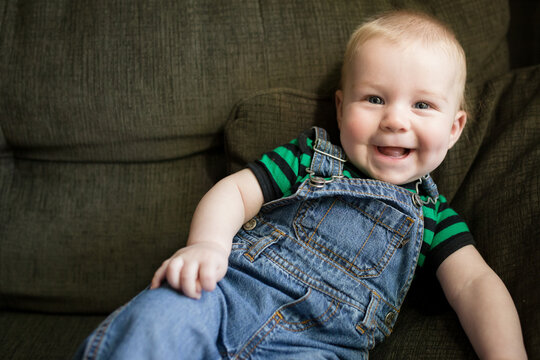 Smiling baby in overalls tips over on couch