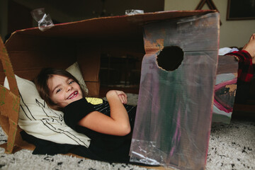little girl lays down inside cardboard box fort