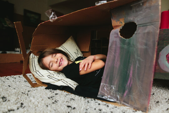 little girl lays down inside cardboard box fort
