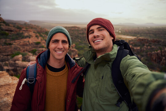 Portrait of handsome male friends taking selfie with backpack while climbing mountain