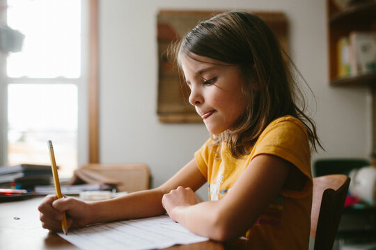Close-up of girl sitting at table at home writing on paper with pencil