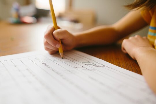 Close-up of girl sitting at table at home writing on paper with pencil