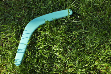 Turquoise wooden boomerang on green grass outdoors, above view. Space for text