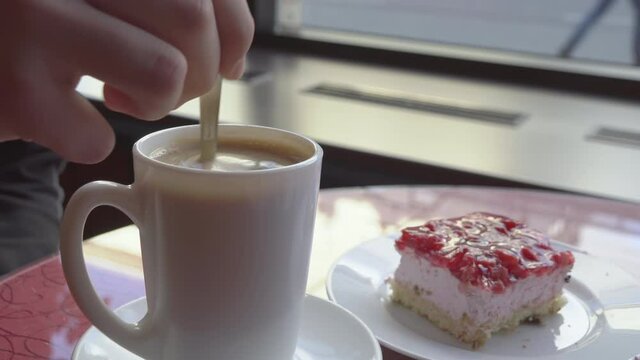 Closeup shot of someone stirring coffee in a cafe. A piece of cake in the background. Amazing leisure activity.