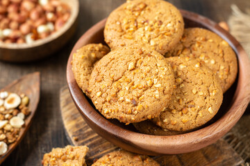 Healthy homemade oatmeal cookies with peanuts in a wooden bowl on a brown kitchen table closeup