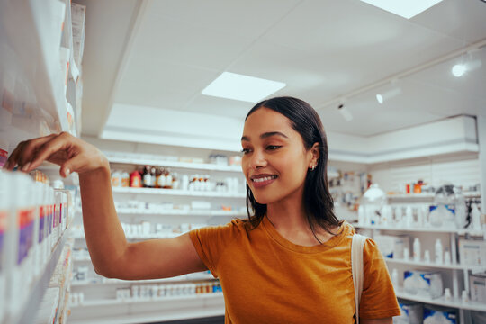 Portrait of smiling young woman in drugstore standing against shelf picking medicine