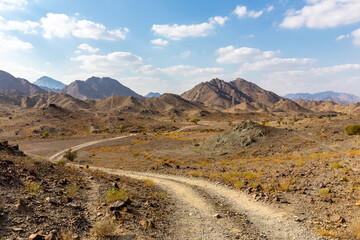 Copper Hike trail, winding gravel dirt road through Wadi Ghargur riverbed and rocky limestone Hajar Mountains in Hatta, United Arab Emirates. - Powered by Adobe