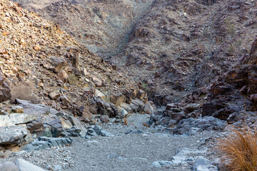 Stony, dry riverbed (wadi) with remains of raw ore of copper, green stones and rocks, Copper Hike Trail, Hatta, Hajar Mountains, UAE.