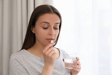 Young woman with glass of water taking pill at home - obrazy, fototapety, plakaty