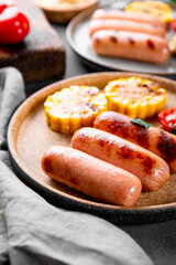  Grilled sausages with vegetables and sauces. Summer BBQ with sausages, corn and tomatoes close up, vertical photo with soft focus
